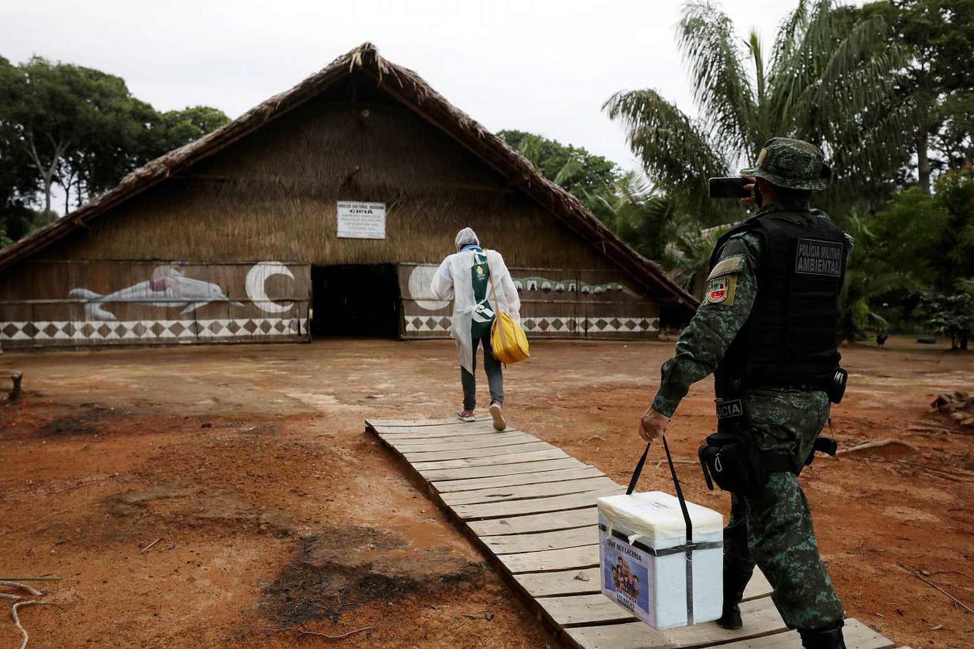 A municipal health worker and an environmental military police officer carry the AstraZeneca/Oxford vaccine to an Indigenous hut in Manaus, Brazil. - REUTERS/Bruno Kelly