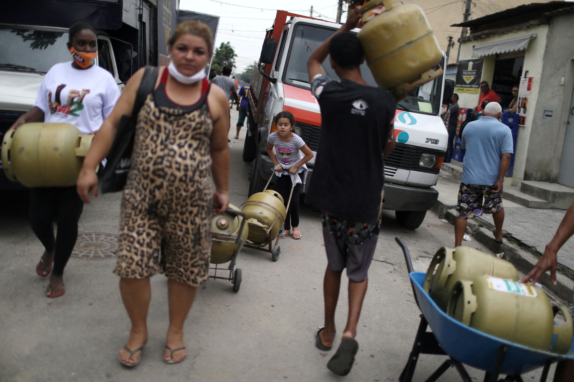 Residents carry cooking gas cylinders after buying them at a fair price in Vila Vintém slum, Rio. REUTERS/Pilar Olivares